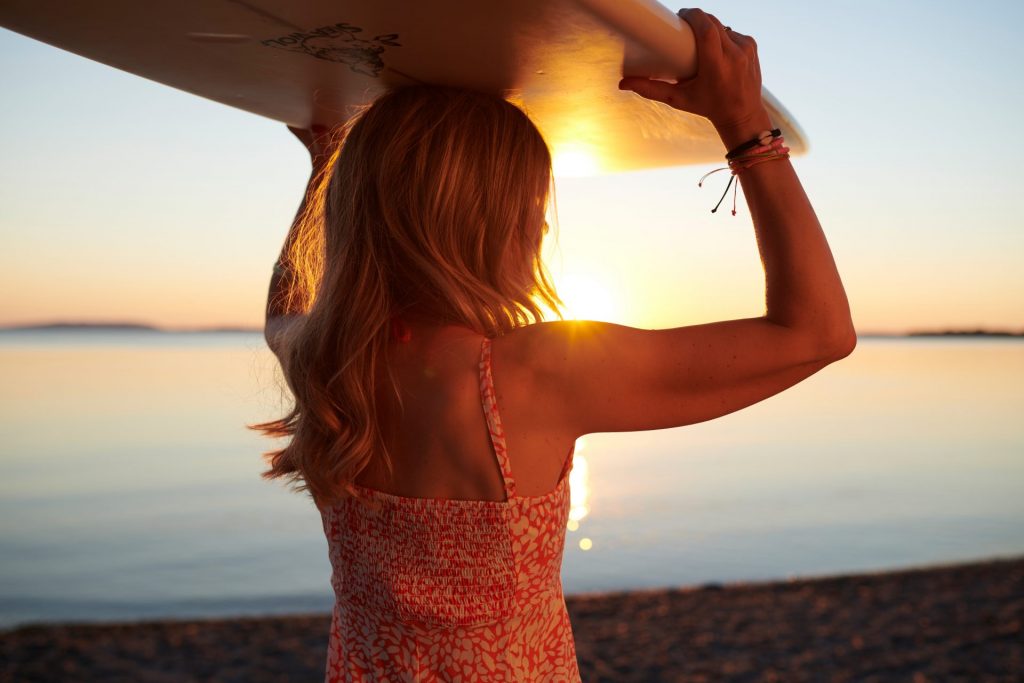 Spirituelle Lehrerin und Abenteurerin mit Surfbrett am See im Sonnenuntergang